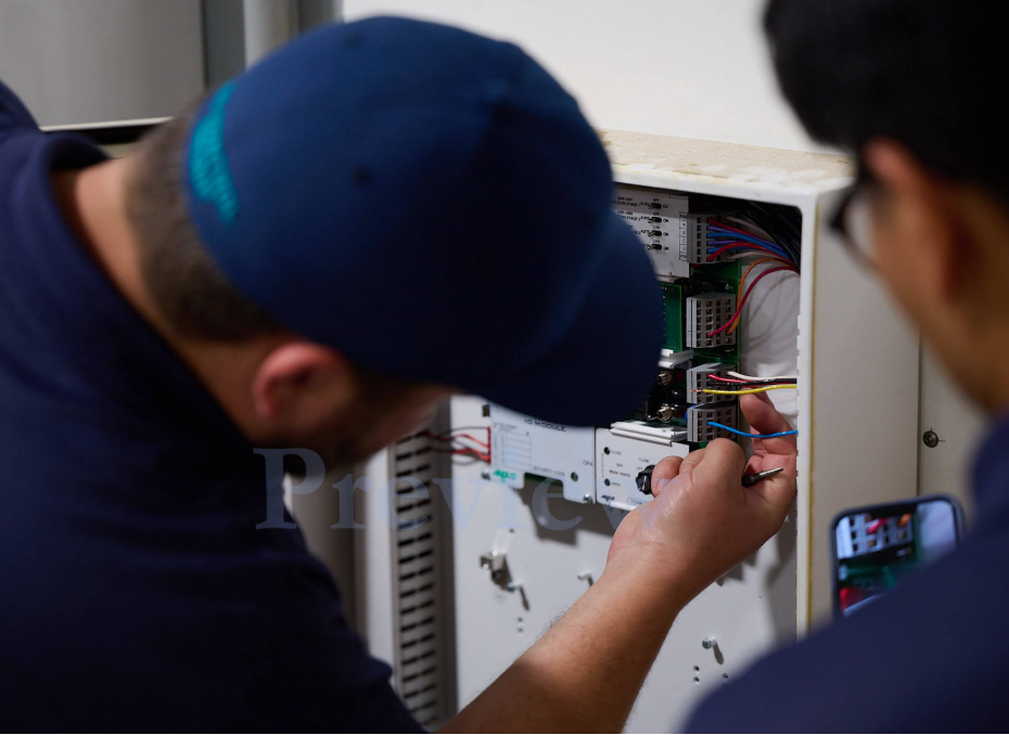 Close-up of TC Controls technicians terminating field wiring and verifying the expansion I/O module