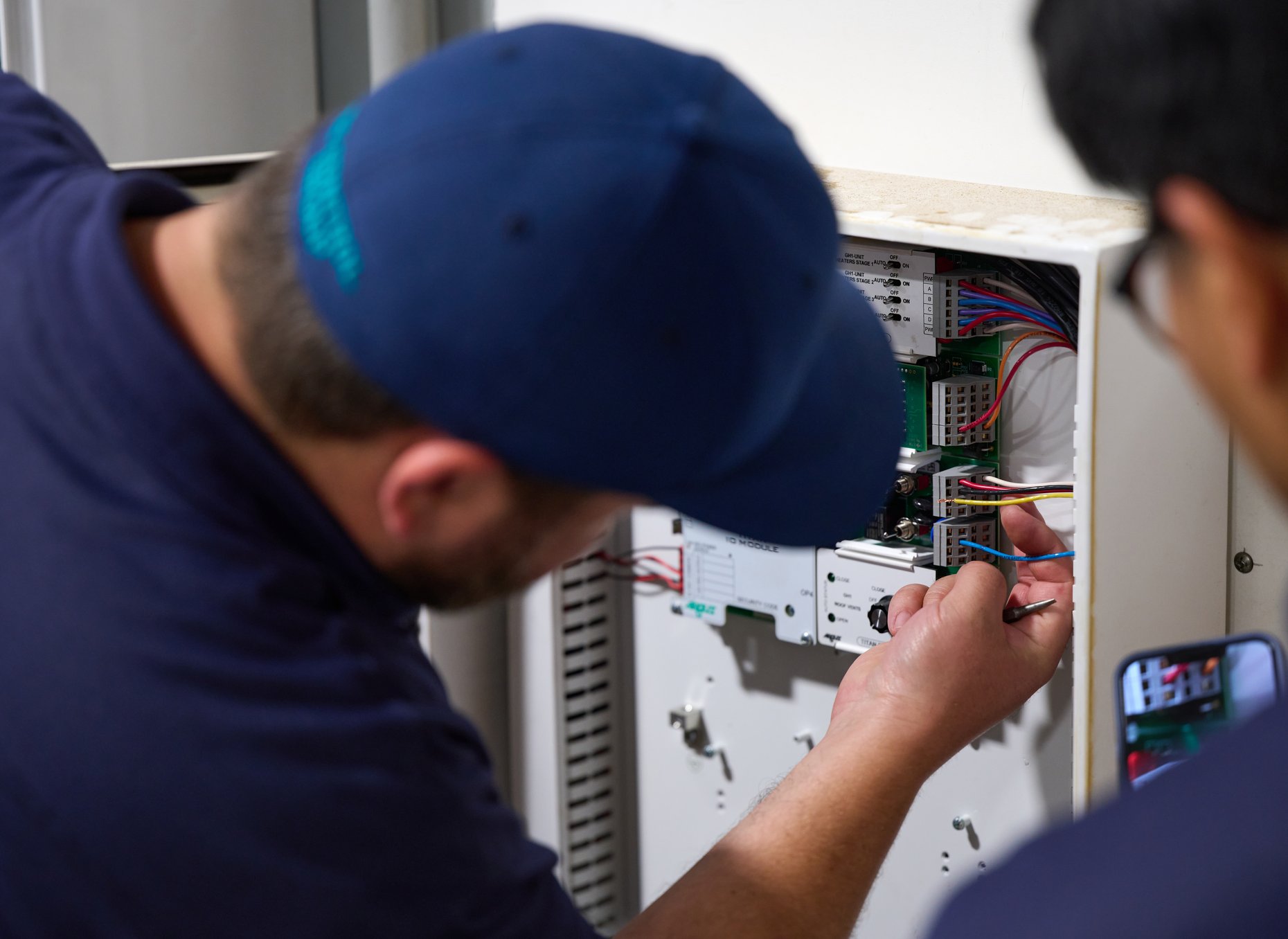 Close-up of TC Controls technicians terminating field wiring and verifying the expansion I/O module